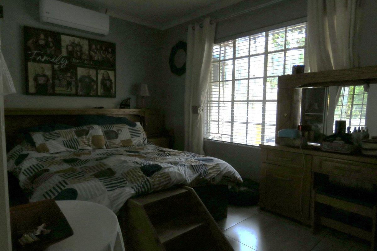 A bedroom featuring tiled flooring, a wall-mounted air conditioning unit, and a large window with security bars.