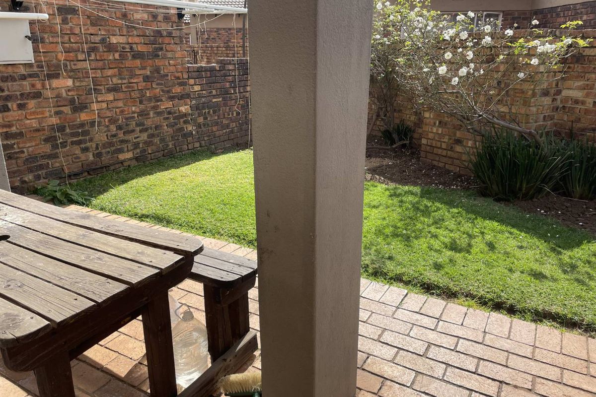 A private rear garden featuring a paved patio area, a small lawn, and perimeter brick boundary walls.