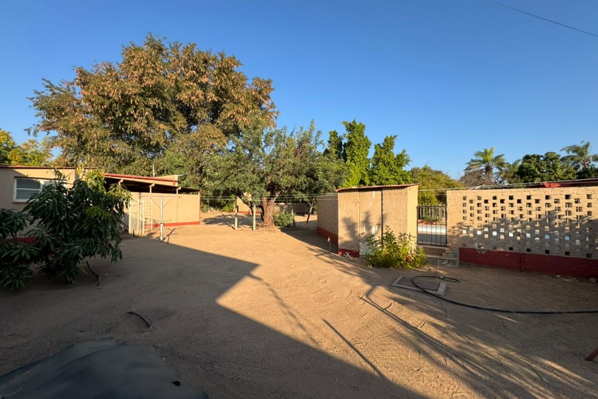 A spacious rear yard featuring a sandy ground surface, a breeze block boundary wall, and a small outbuilding structure.
