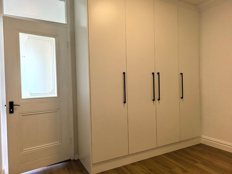 A clean, modern bedroom featuring light timber flooring and a large, white built-in wardrobe with contemporary black handles.