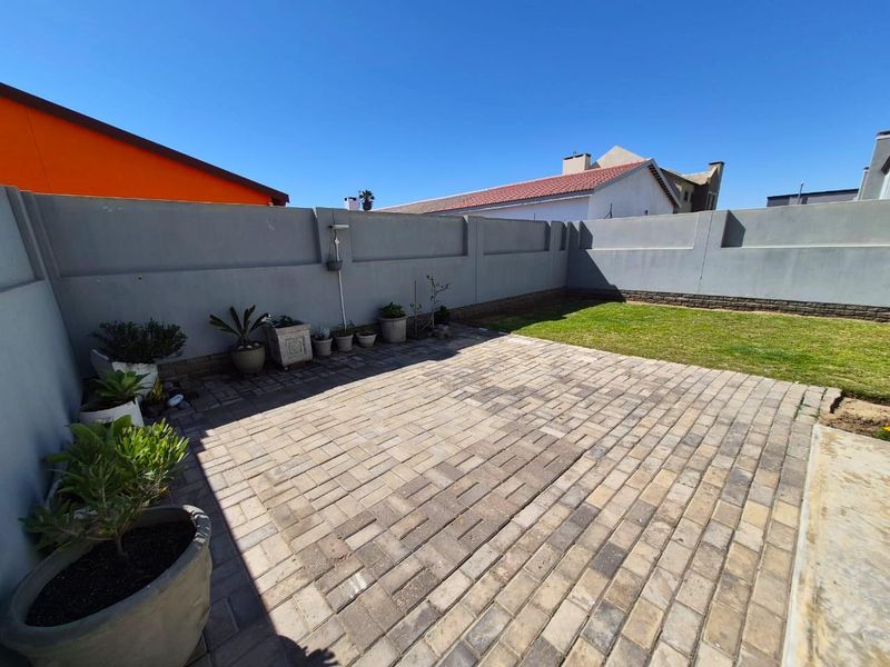 A private rear courtyard featuring a paved patio area and a small lawn, enclosed by solid boundary walls.