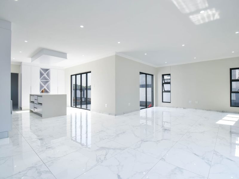 Spacious open-plan living and kitchen area featuring high-gloss marble-look floor tiles, modern built-in cabinetry, and large glass doors leading to the exterior.