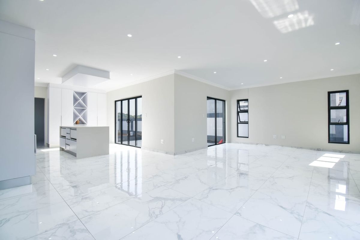 Spacious open-plan living and kitchen area featuring high-gloss marble-look floor tiles, modern built-in cabinetry, and large glass doors leading to the exterior.