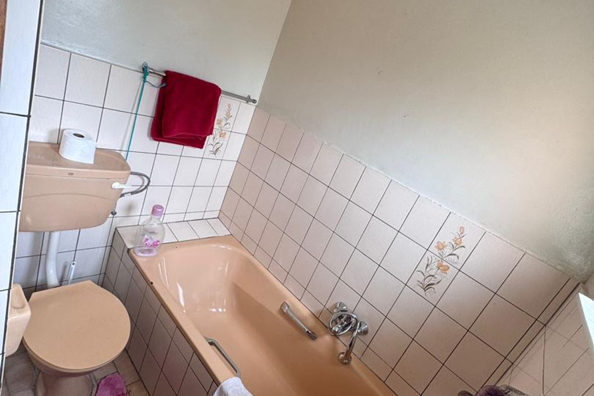 A compact bathroom featuring a vintage peach-colored bathtub, matching toilet, and tiled walls, offering a dated aesthetic ready for modernization.