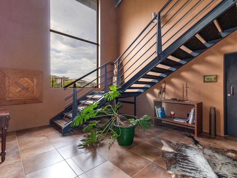 Spacious entrance hall featuring a modern metal staircase, large floor-to-ceiling window providing natural light, and durable tiled flooring.