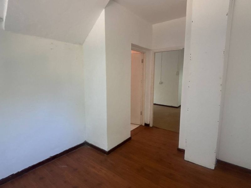 An empty bedroom featuring laminate flooring and a window with security bars, requiring minor cosmetic updates to the walls.