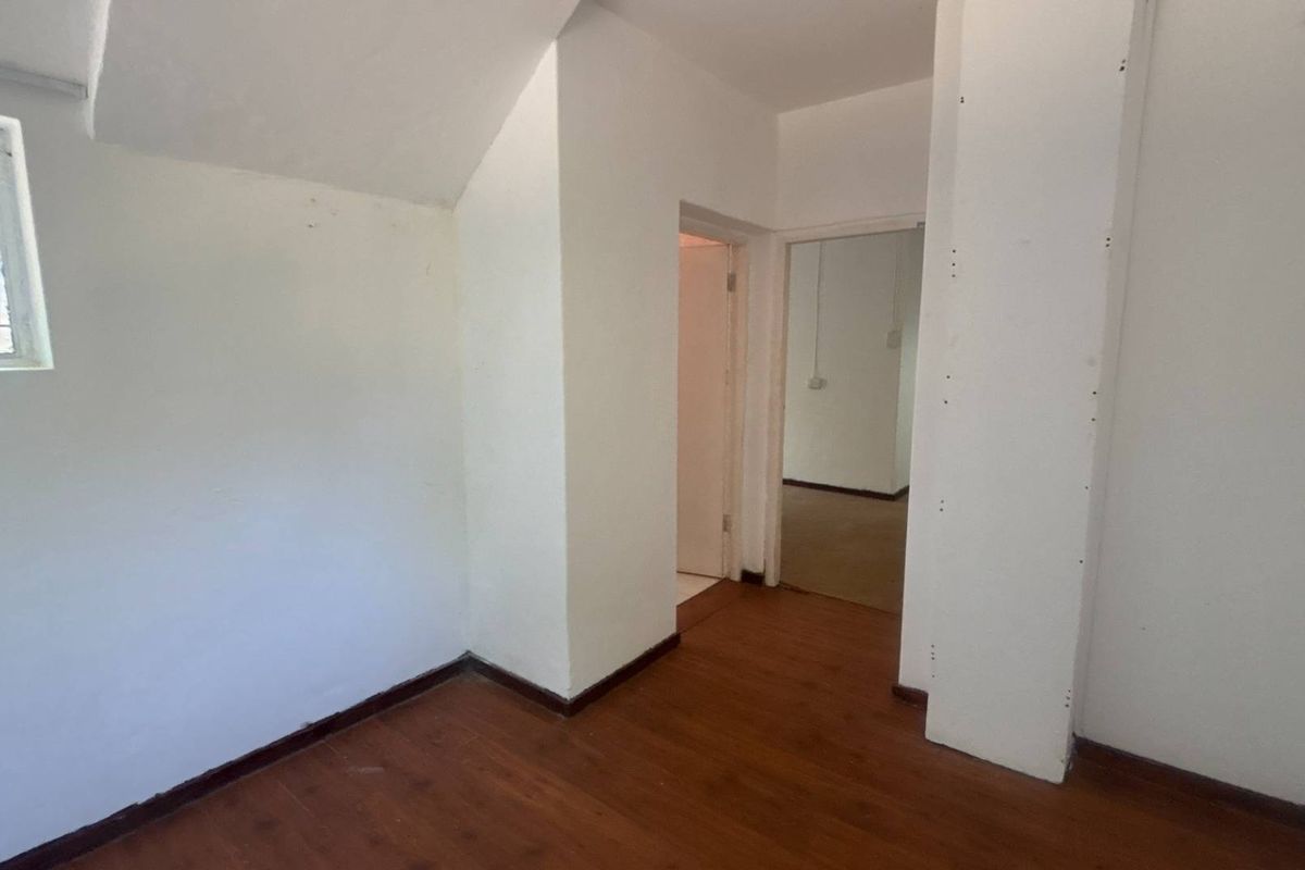 An empty bedroom featuring laminate flooring and a window with security bars, requiring minor cosmetic updates to the walls.