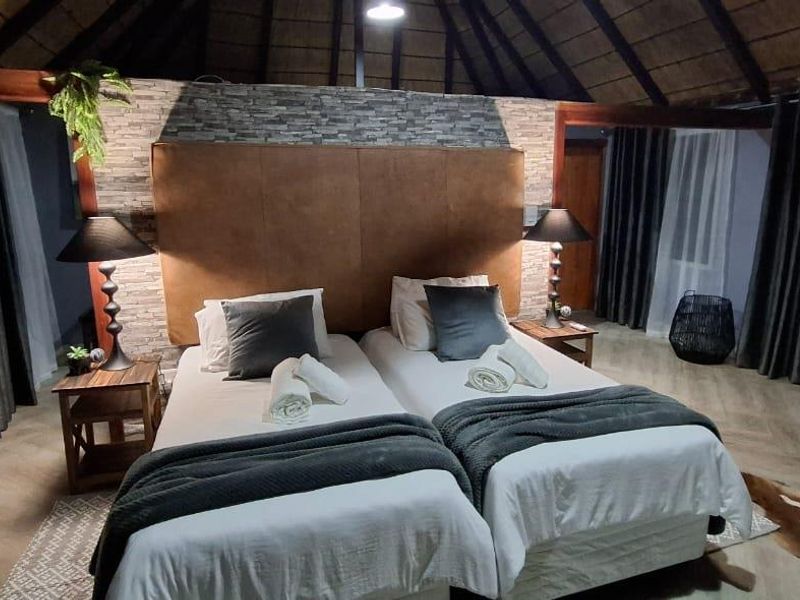 A well-maintained bedroom featuring a high thatched ceiling with exposed rafters, a stone veneer feature wall, and modern herringbone flooring.