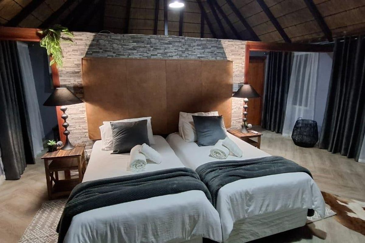 A well-maintained bedroom featuring a high thatched ceiling with exposed rafters, a stone veneer feature wall, and modern herringbone flooring.