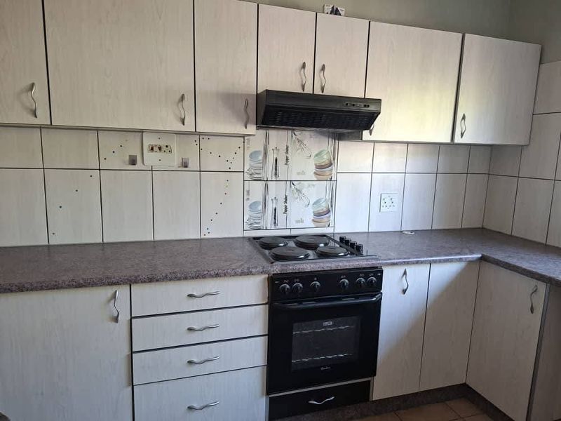A functional kitchen featuring light-toned laminate cabinetry, stone-look countertops, a built-in electric stove with extractor fan, and a decorative tiled backsplash.