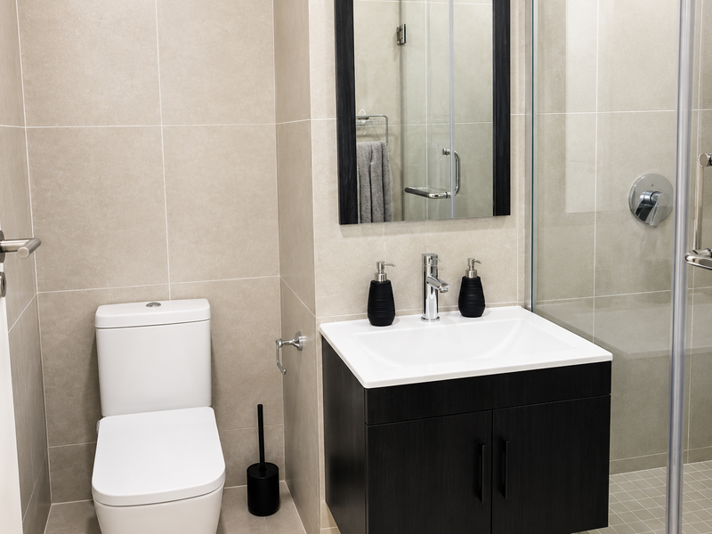 Modern bathroom featuring a wall-mounted vanity, ceramic basin, back-to-wall toilet, and a glass-enclosed shower with neutral wall tiling.