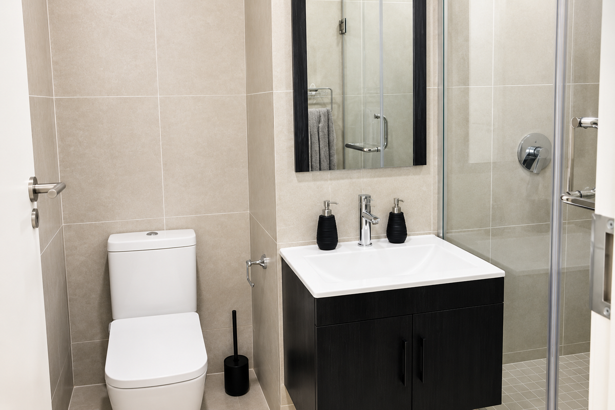 Modern bathroom featuring a wall-mounted vanity, ceramic basin, back-to-wall toilet, and a glass-enclosed shower with neutral wall tiling.