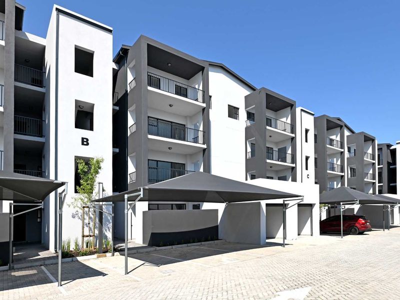 Modern multi-story apartment complex featuring contemporary architectural design, private balconies with metal railings, and dedicated shade cloth parking bays.