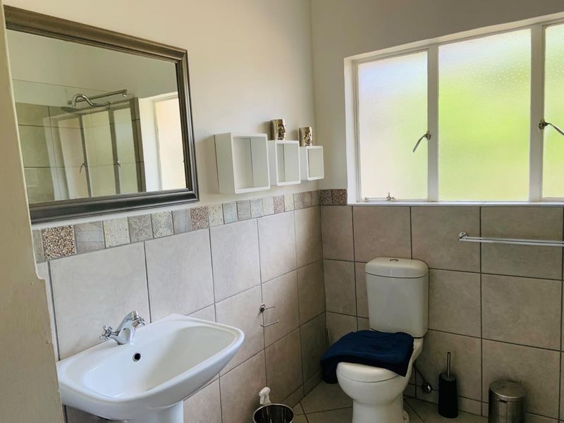 A functional bathroom featuring a pedestal basin, toilet, tiled walls, and a window providing natural light.