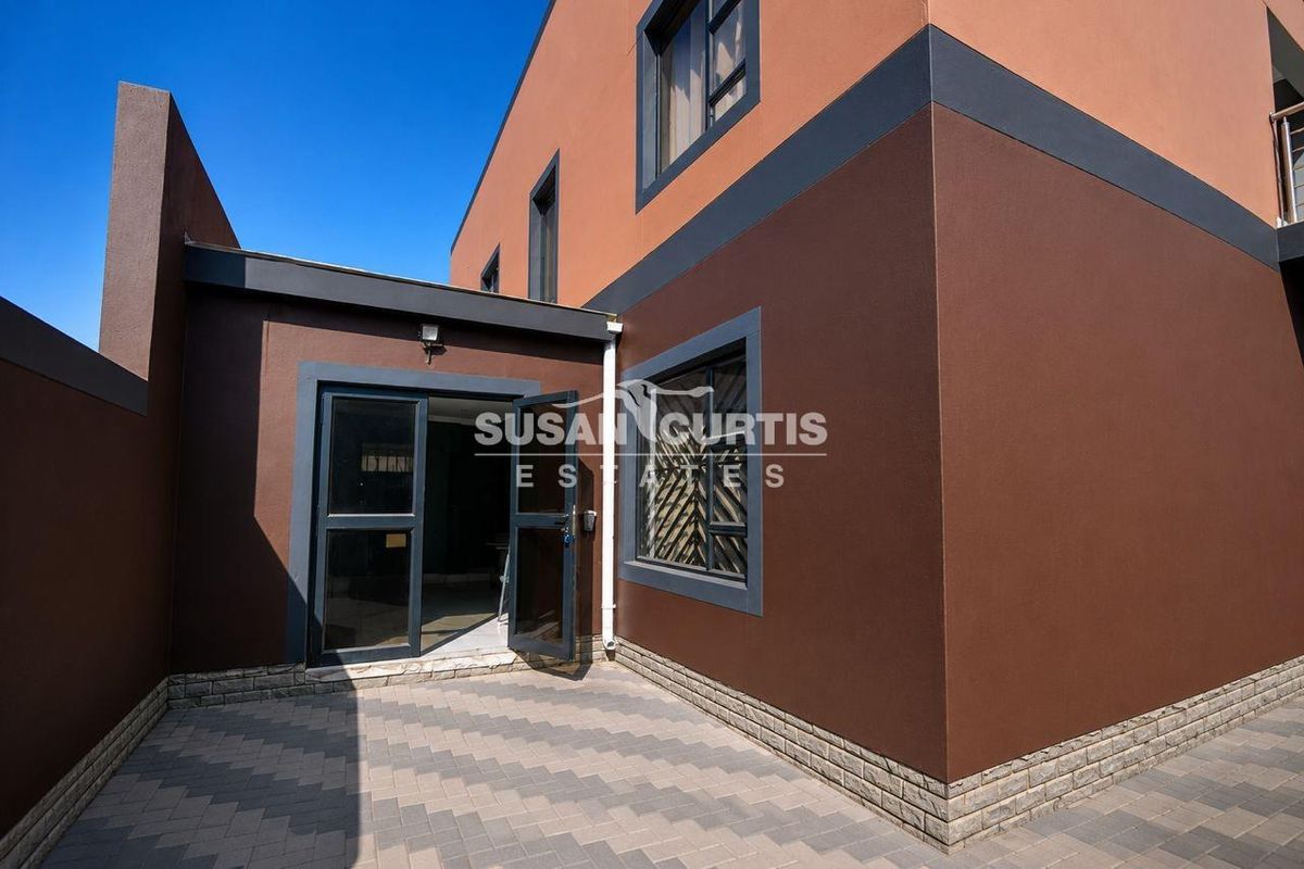 Rear exterior view of the property featuring a paved courtyard, modern dark-toned facade, and glass-panelled door access.