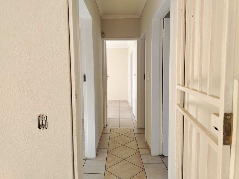 A vacant residential hallway featuring tiled flooring and a security gate, showing signs of wear and requiring minor cosmetic maintenance.