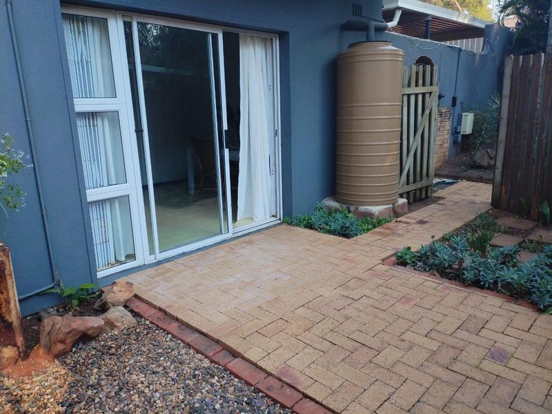 Rear exterior view of the cottage featuring a paved patio area, sliding glass door access, and a functional water tank installation.
