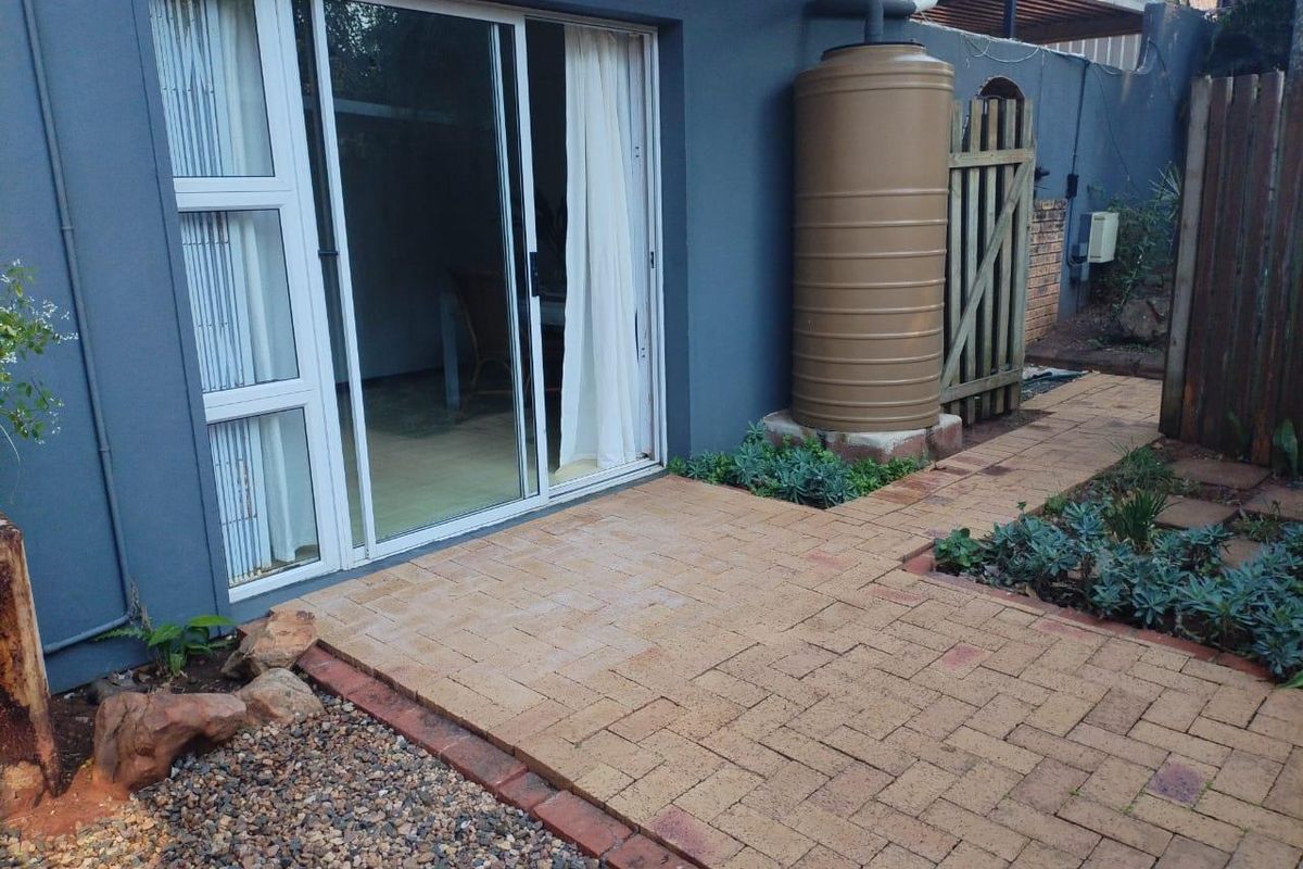 Rear exterior view of the cottage featuring a paved patio area, sliding glass door access, and a functional water tank installation.