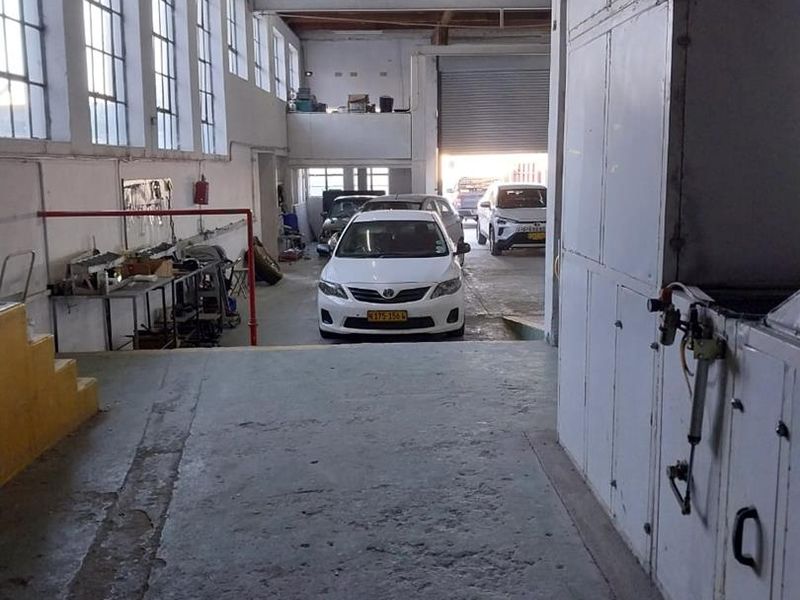 Spacious industrial garage featuring exposed timber roof trusses, large windows for natural light, concrete flooring, and a large roller shutter door for vehicle access.