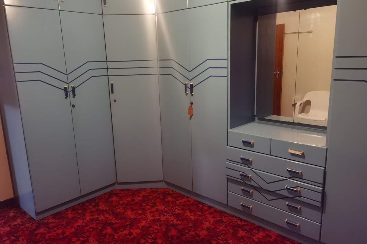 Bedroom featuring extensive built-in cabinetry with integrated vanity and mirror, finished with dated blue detailing and red patterned carpeting.