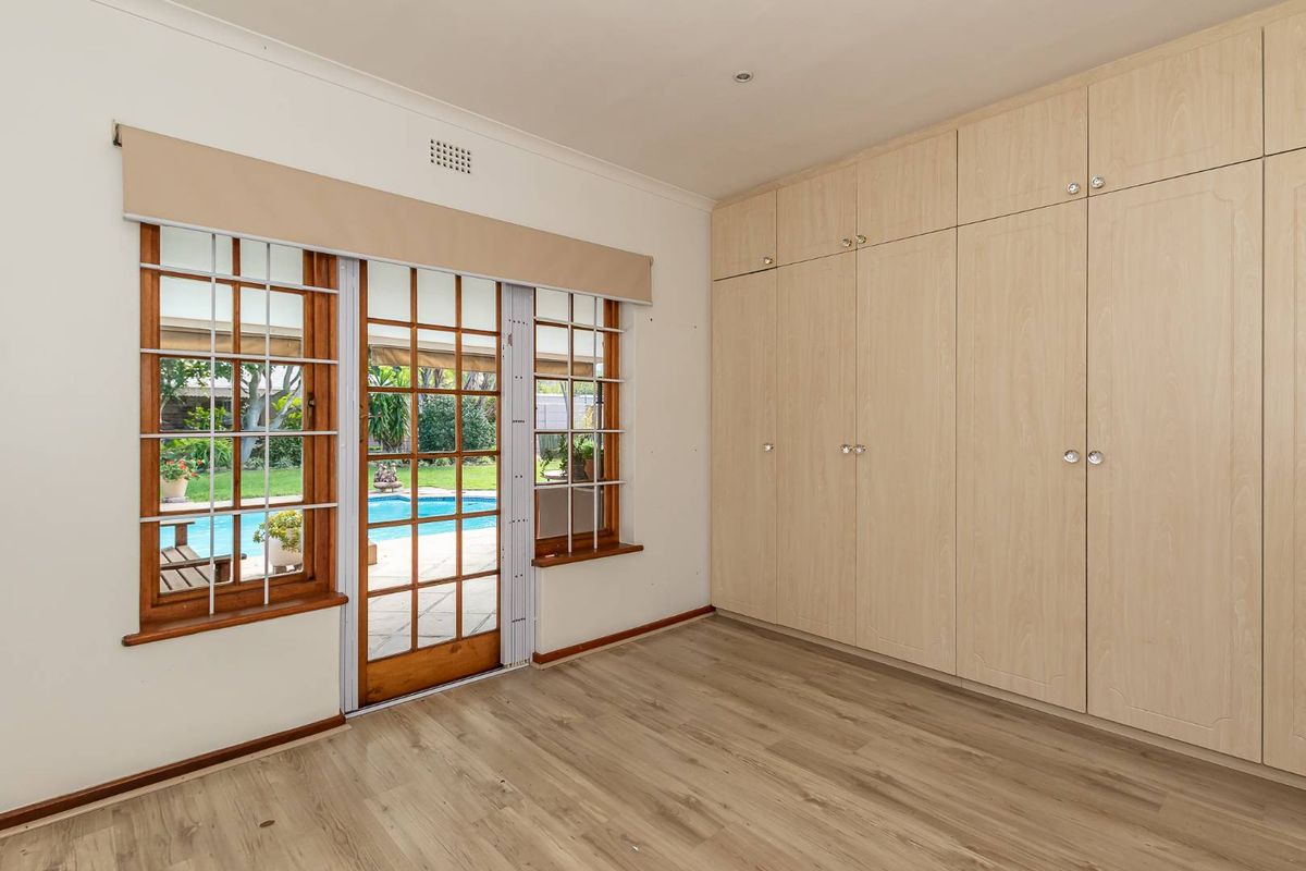 A bright bedroom featuring light wood-look flooring, extensive built-in cabinetry, and a wooden sliding door providing direct access to the pool area.