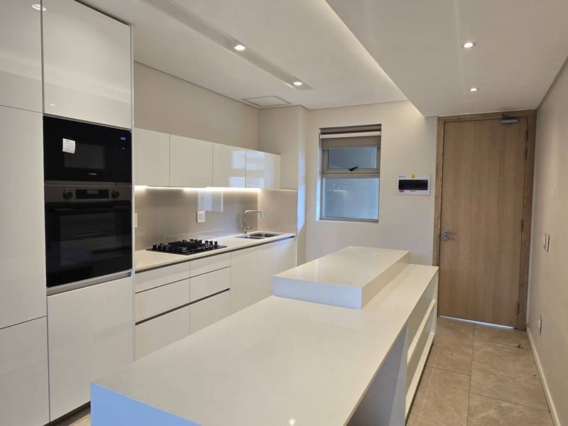 Modern kitchen featuring high-gloss cabinetry, stone countertops, a central island, integrated appliances, and recessed lighting in a clean, contemporary finish.