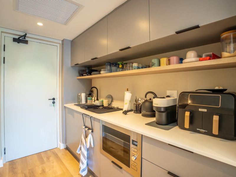 A modern, compact kitchen featuring sleek grey cabinetry, stone countertops, a built-in microwave, and high-quality finishes throughout.