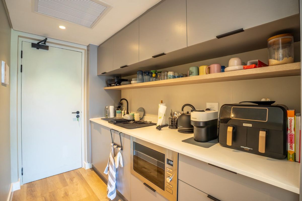 A modern, compact kitchen featuring sleek grey cabinetry, stone countertops, a built-in microwave, and high-quality finishes throughout.