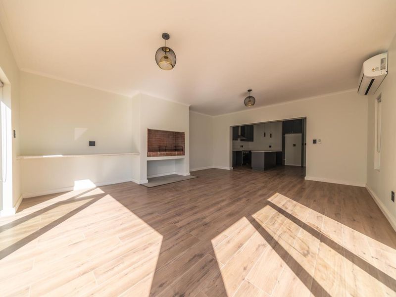 Spacious open-plan living area featuring wood-look tile flooring, a built-in fireplace, and a split-system air conditioner, with a view into the adjacent kitchen.