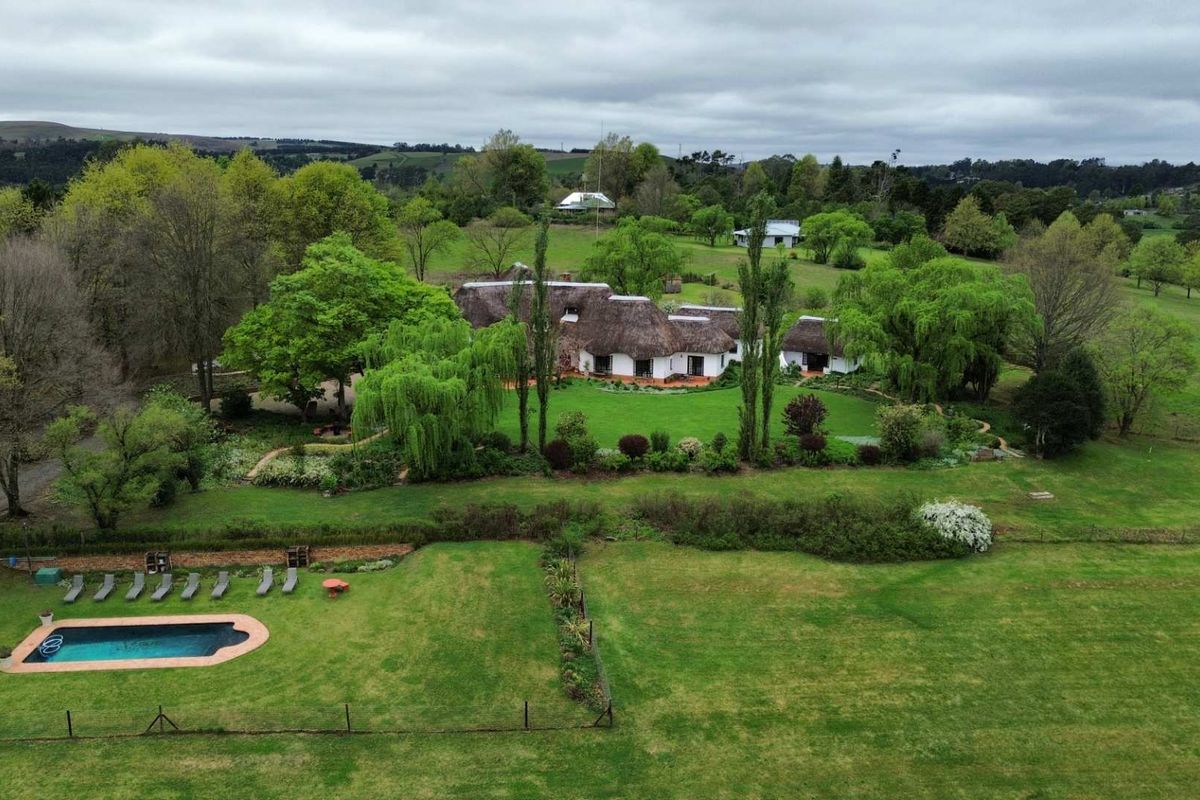 Aerial view of a rural property featuring a traditional thatched-roof house, expansive landscaped gardens, and a private swimming pool set in a scenic landscape.