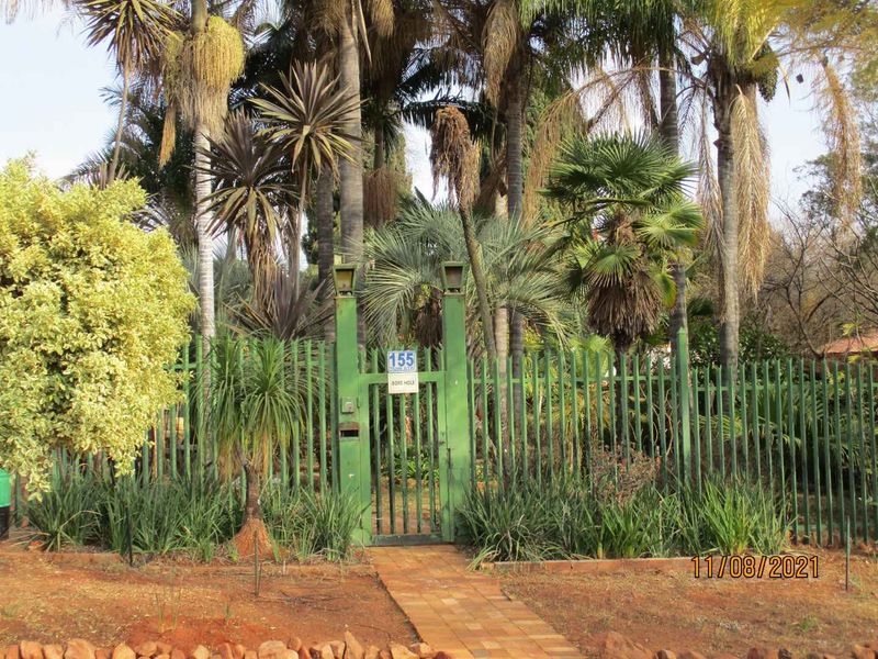 Front entrance view featuring a green metal security fence, pedestrian gate, and a brick paved pathway leading to the property.