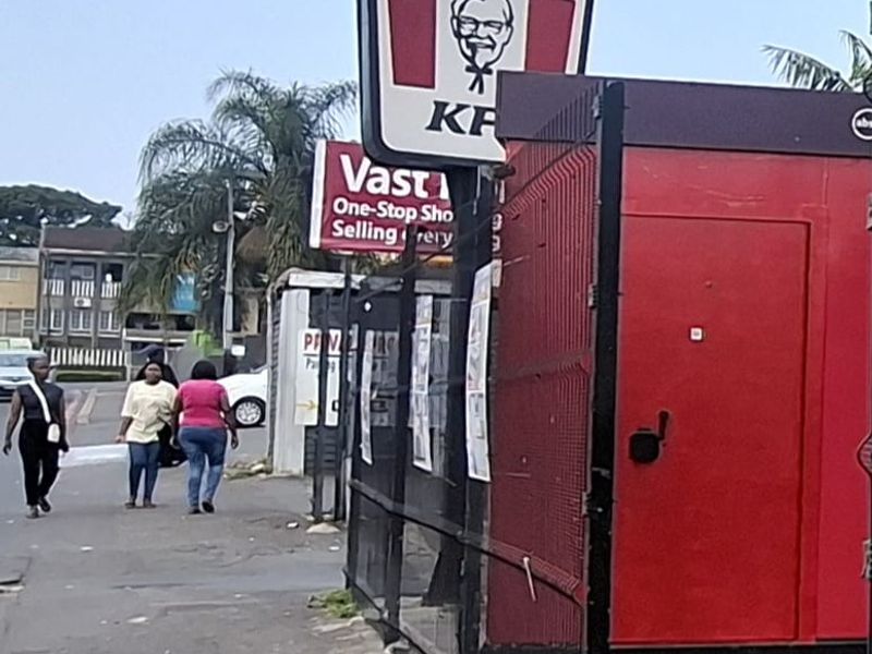 Exterior view of a commercial property featuring branded signage and security fencing along a paved pedestrian walkway.
