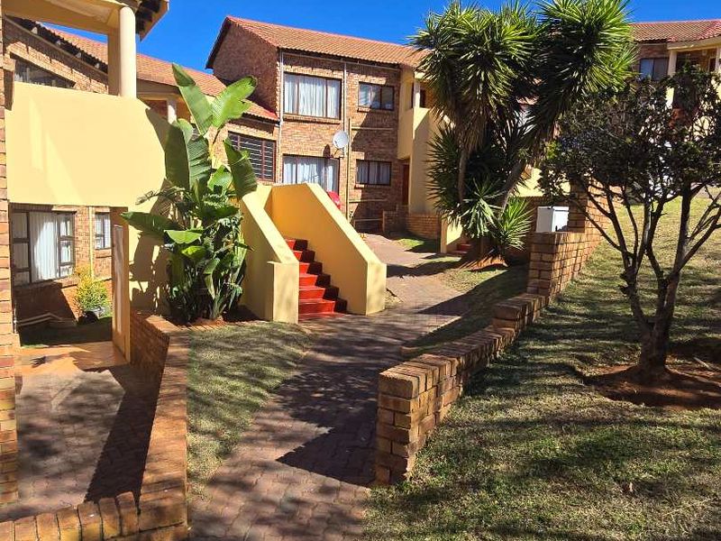 Exterior view of a townhouse complex featuring brick paved pathways, retaining walls, and a concrete staircase leading to upper-level units.