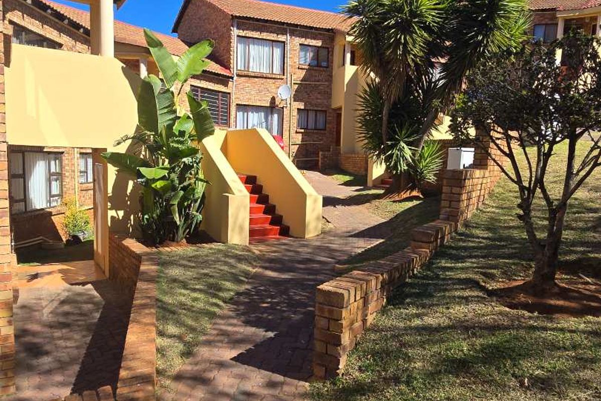 Exterior view of a townhouse complex featuring brick paved pathways, retaining walls, and a concrete staircase leading to upper-level units.