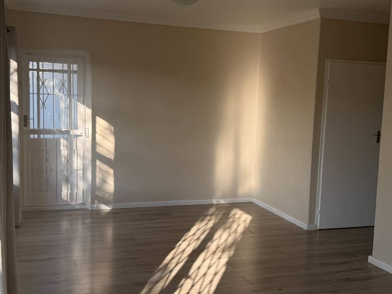 A bright, empty living area featuring modern laminate flooring, neutral wall tones, and a secure metal entrance gate.