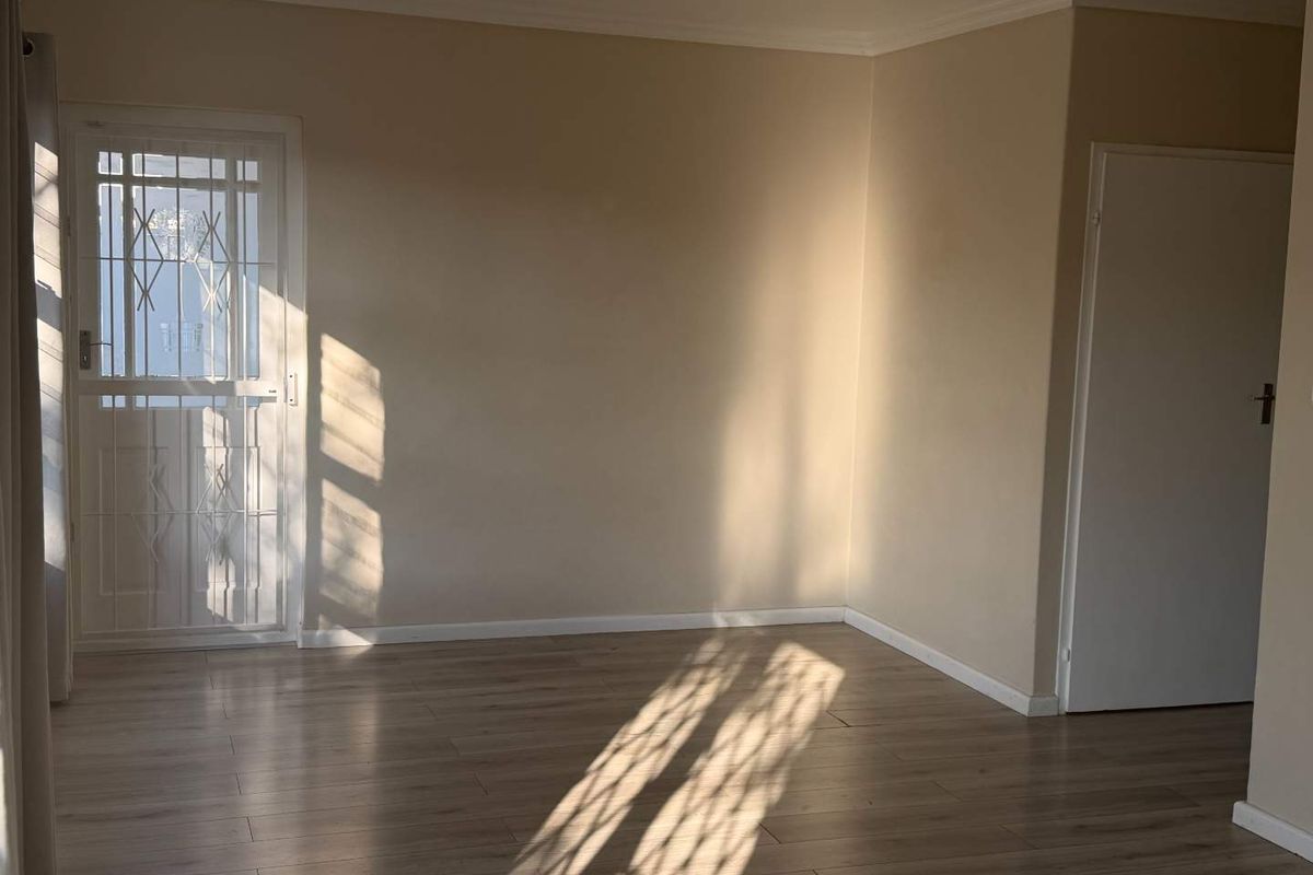 A bright, empty living area featuring modern laminate flooring, neutral wall tones, and a secure metal entrance gate.