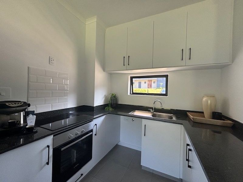 Modern kitchen featuring white cabinetry, contrasting black granite countertops, subway tile backsplash, and integrated stainless steel oven and cooktop.