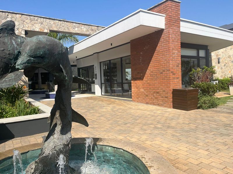 A modern apartment complex entrance featuring a decorative water fountain, brick and stone exterior finishes, and large glass windows.