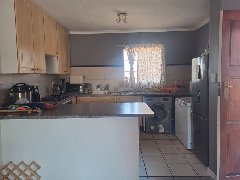 Functional kitchen featuring light wood cabinetry, laminate countertops, tiled backsplash, and integrated laundry plumbing, offering a practical layout for daily use.