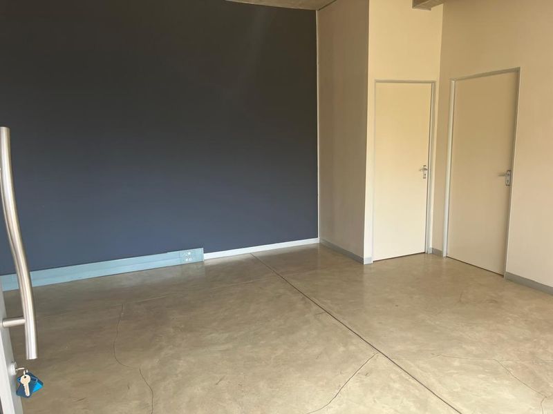 A bright, empty office space featuring polished concrete flooring, a dark accent wall, and two internal doors.