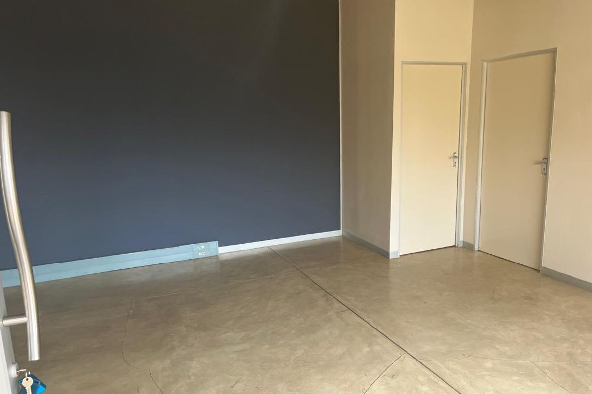 A bright, empty office space featuring polished concrete flooring, a dark accent wall, and two internal doors.