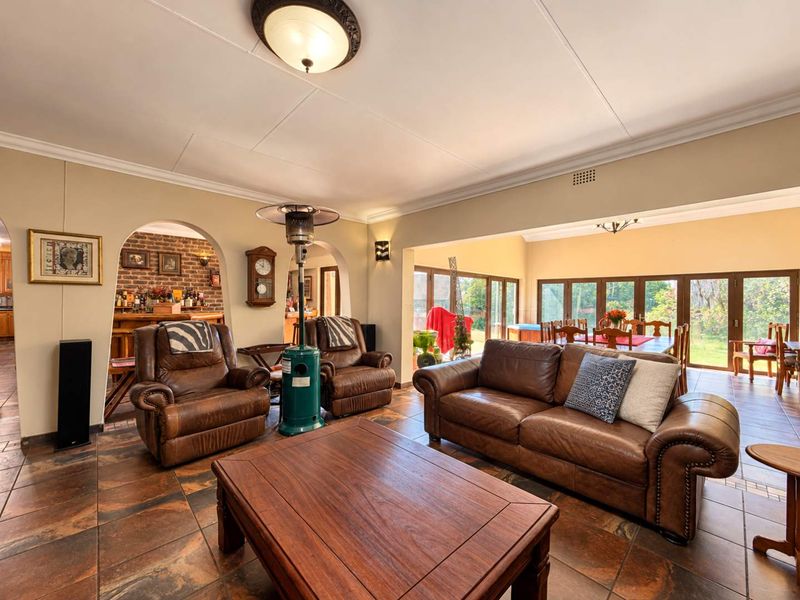 Spacious open-plan living and dining area featuring tiled floors, arched architectural details, exposed brick accents, and large sliding doors providing natural light and garden access.