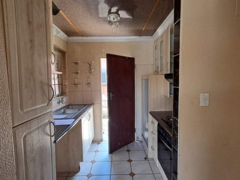 A compact kitchen featuring built-in cabinetry, a built-in oven with hob, and tiled flooring, offering a functional layout in need of cosmetic updates.