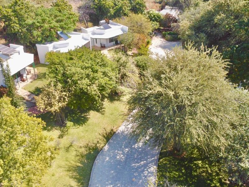 Aerial view of the lodge property featuring multiple white structures with solar water heating systems, surrounded by lush trees and a paved driveway.