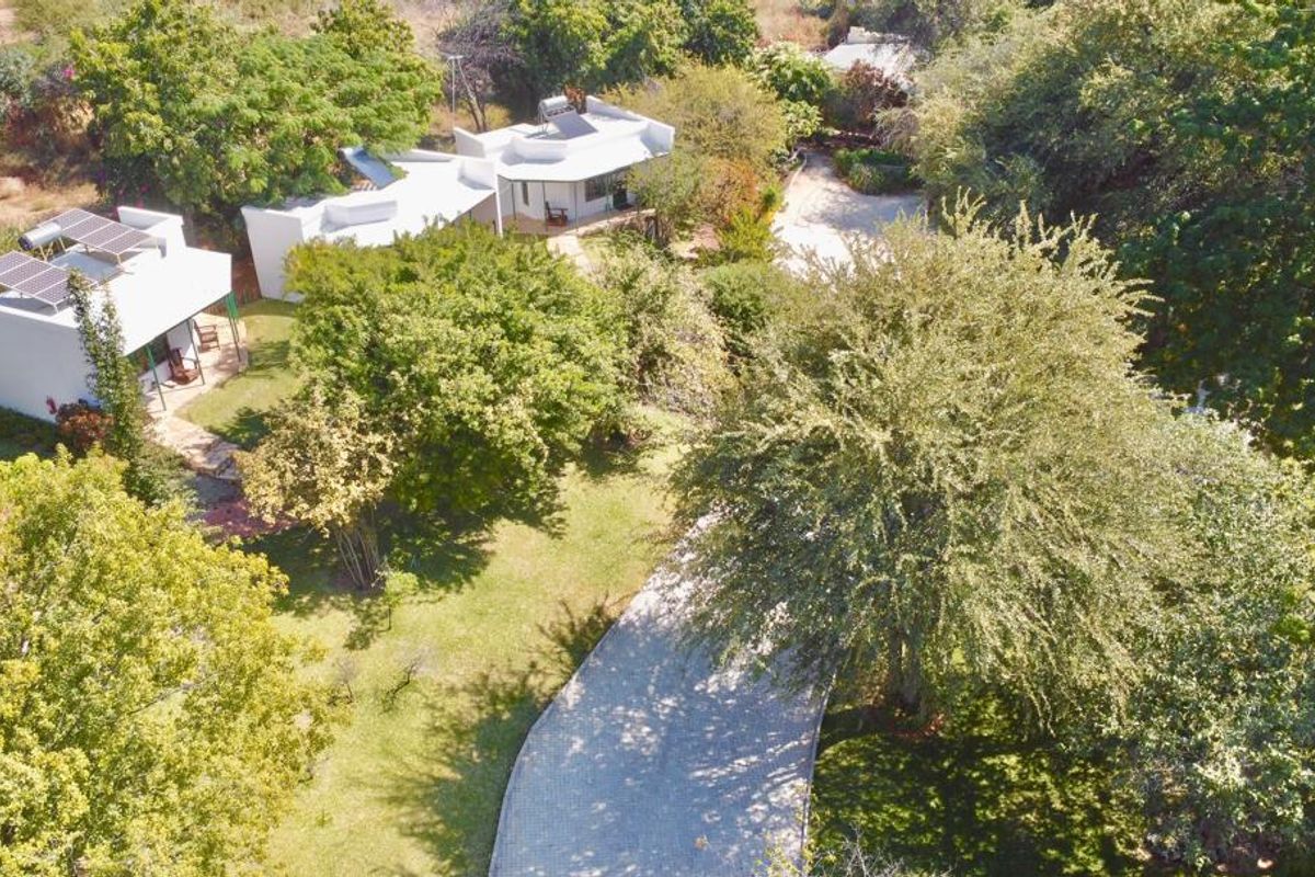 Aerial view of the lodge property featuring multiple white structures with solar water heating systems, surrounded by lush trees and a paved driveway.