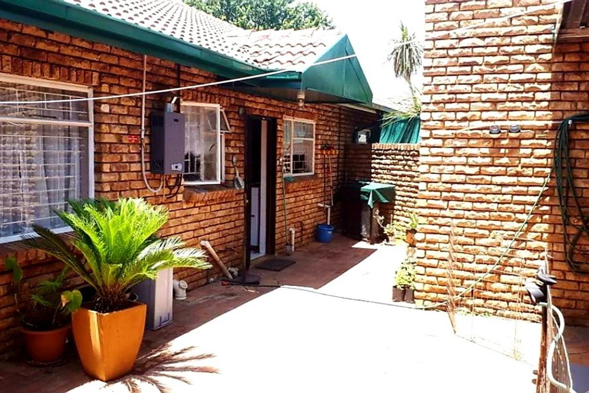 A rear exterior view of a face brick townhouse featuring a paved patio area, gas geyser, and protective security bars on the windows.