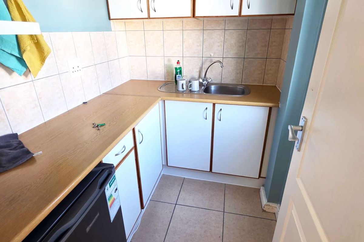A compact kitchenette featuring laminate countertops, built-in cabinetry, a stainless steel sink, and tiled splashbacks.