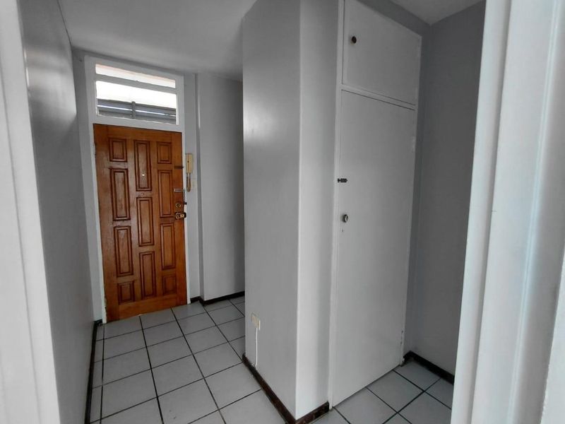 An entrance hallway featuring tiled flooring, a classic wooden front door with a transom window, and a built-in storage cupboard.