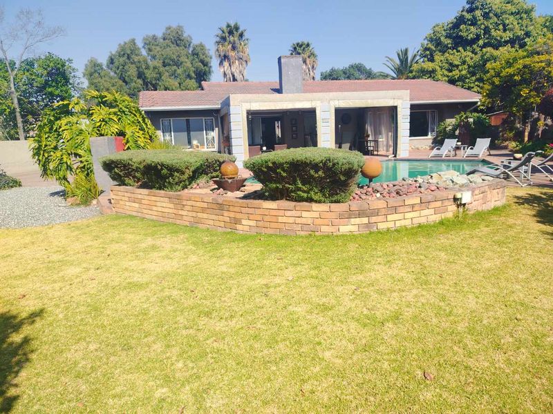 Rear view of the house featuring a swimming pool, a brick retaining wall, and a covered patio area set within a landscaped garden.