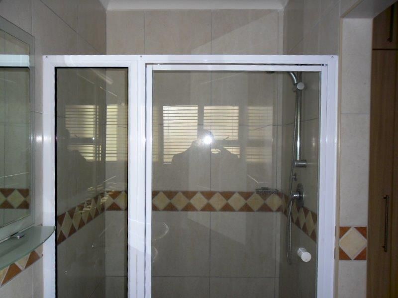 A functional bathroom featuring a glass-enclosed shower with tiled walls and a decorative border, complemented by built-in cabinetry.